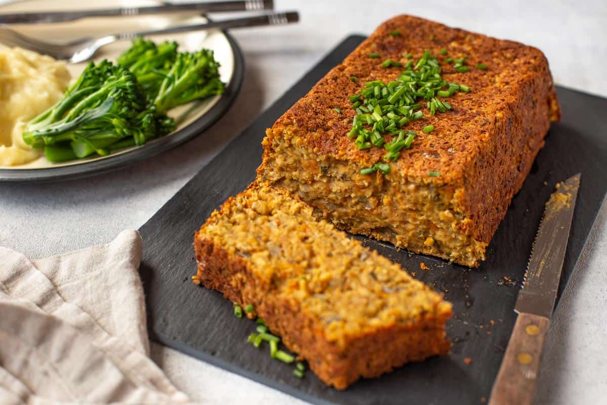 A vegan lentil loaf on a board with a slice cut off.