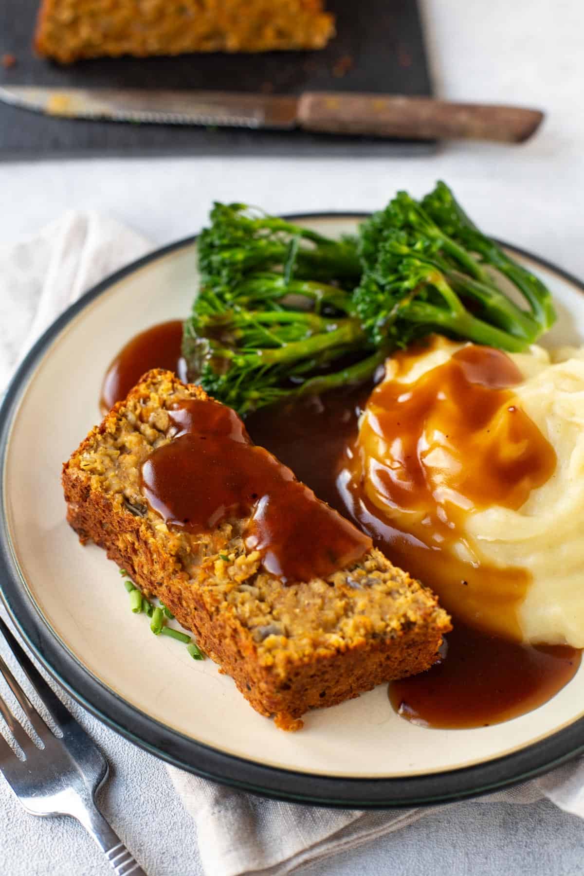 A slice of vegan lentil loaf on a plate with mashed potato, broccoli and gravy.