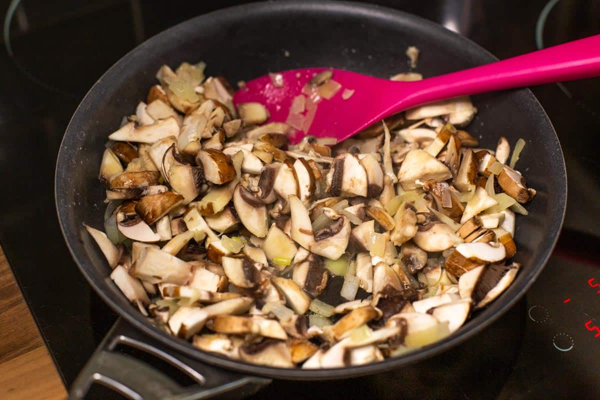 Chopped mushrooms and onions frying in a pan.