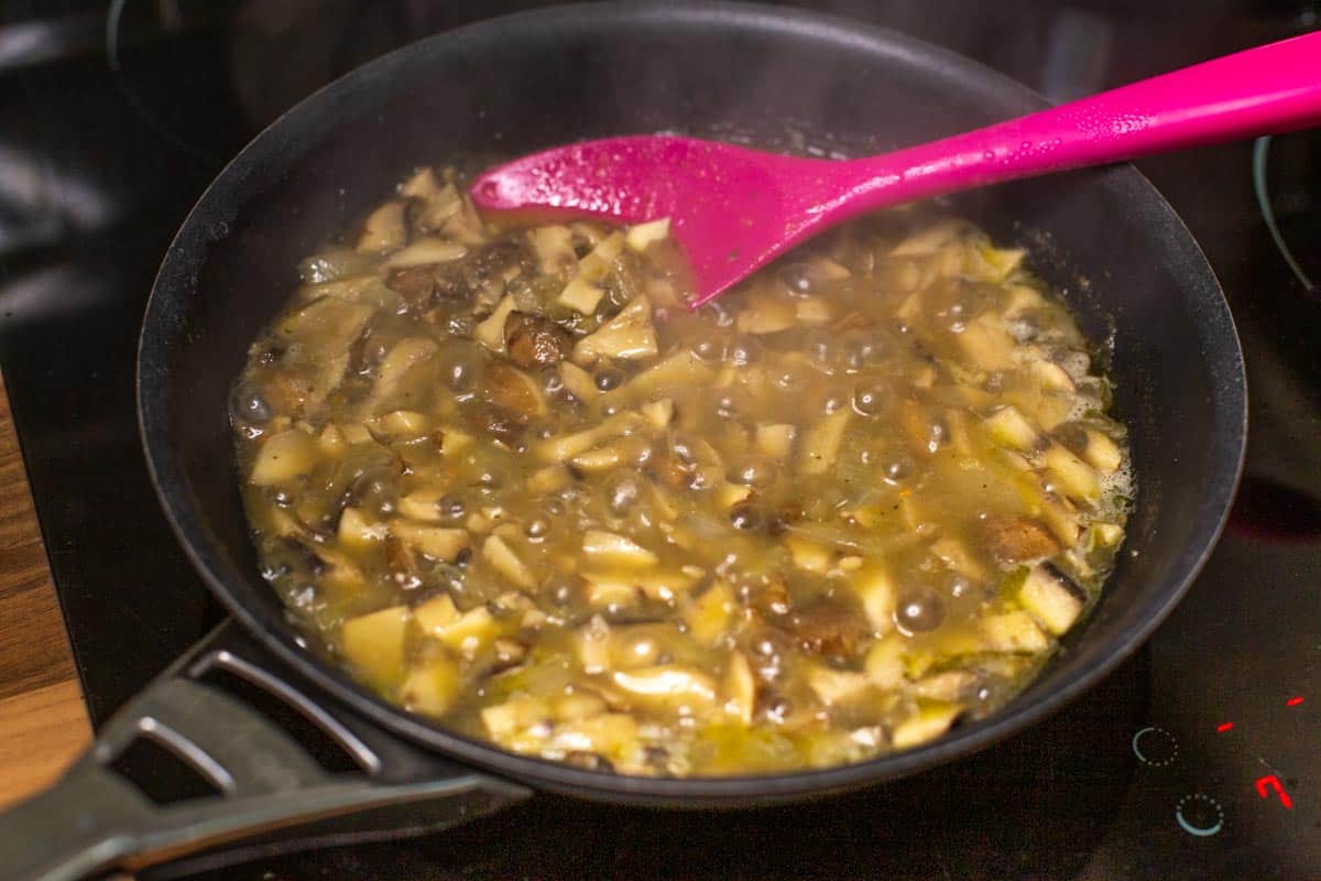 Mushrooms and white wine bubbling in a hot frying pan.