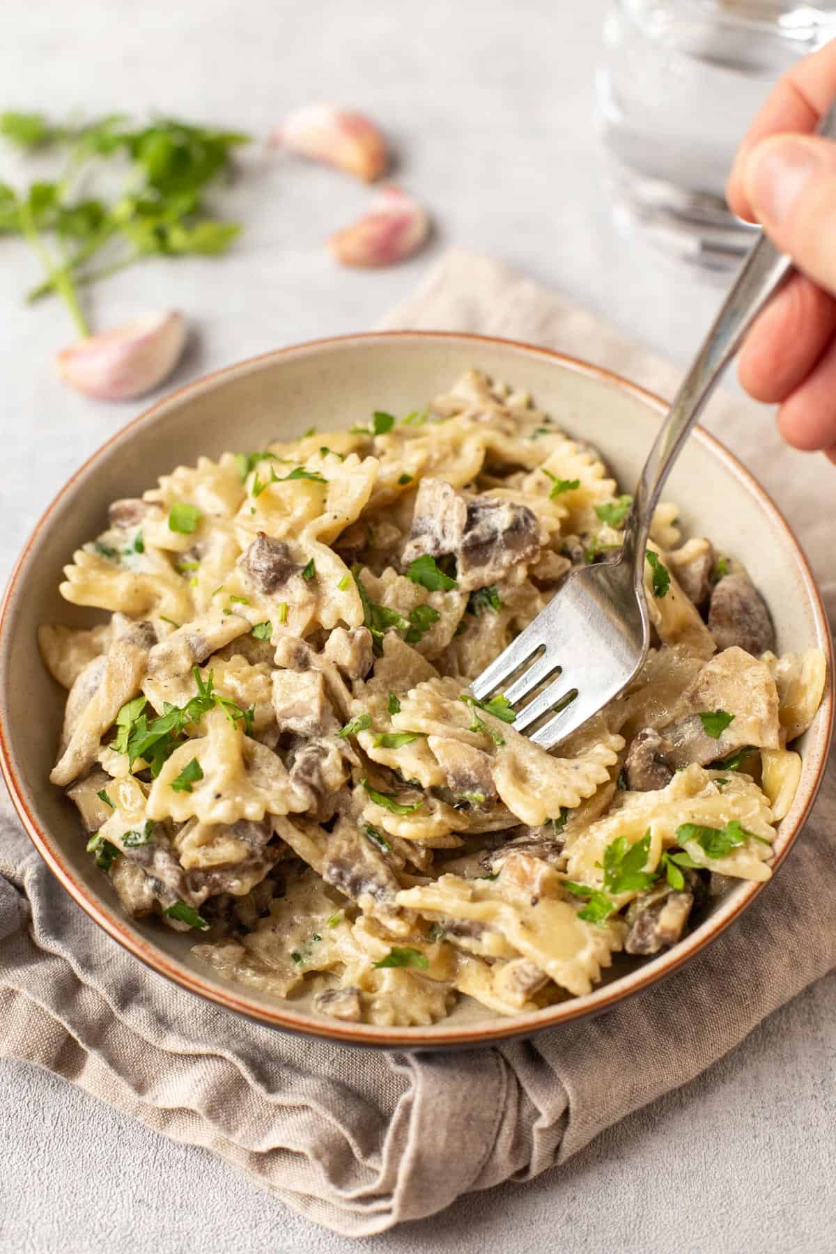 A fork taking a scoop from a bowl of pasta in creamy mushroom and white wine sauce.