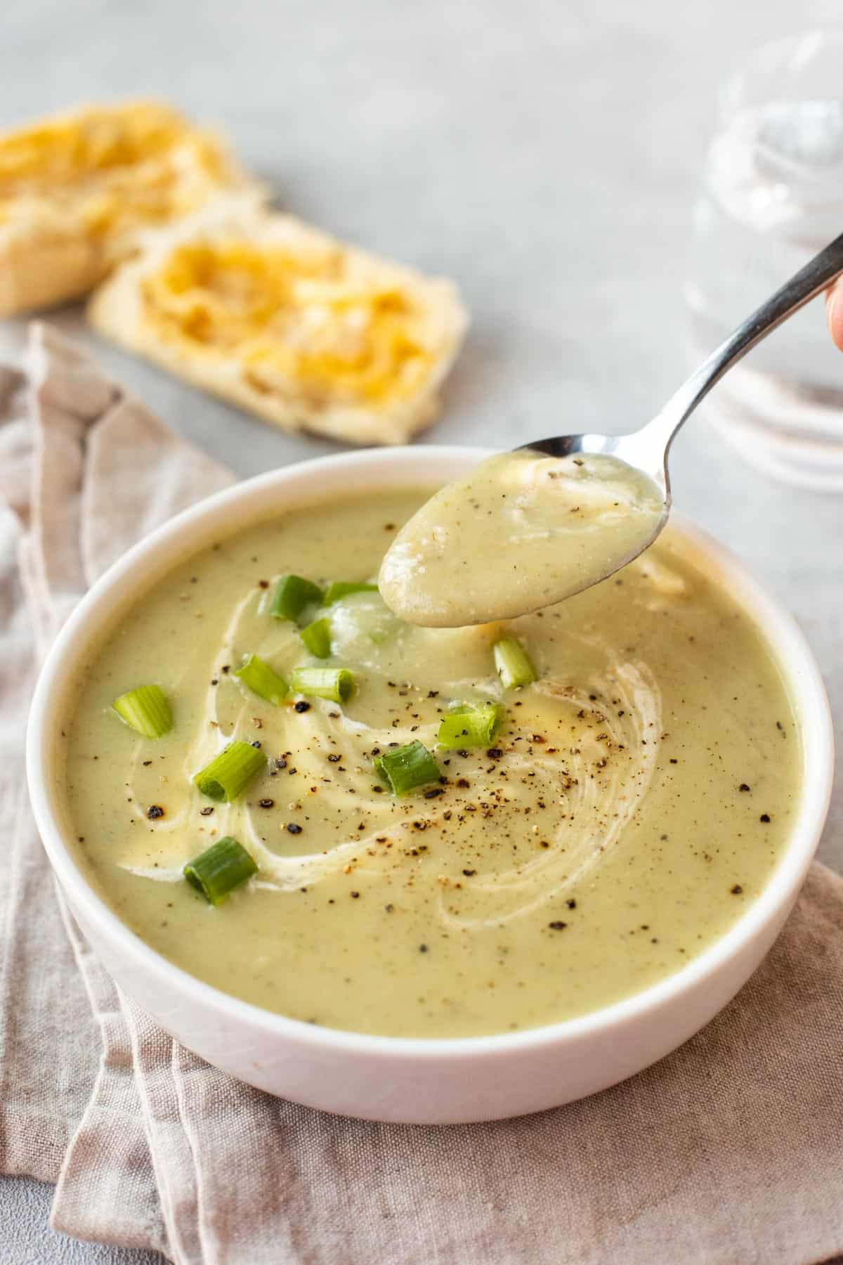 A spoon taking a scoop of a creamy potato and spring onion soup.