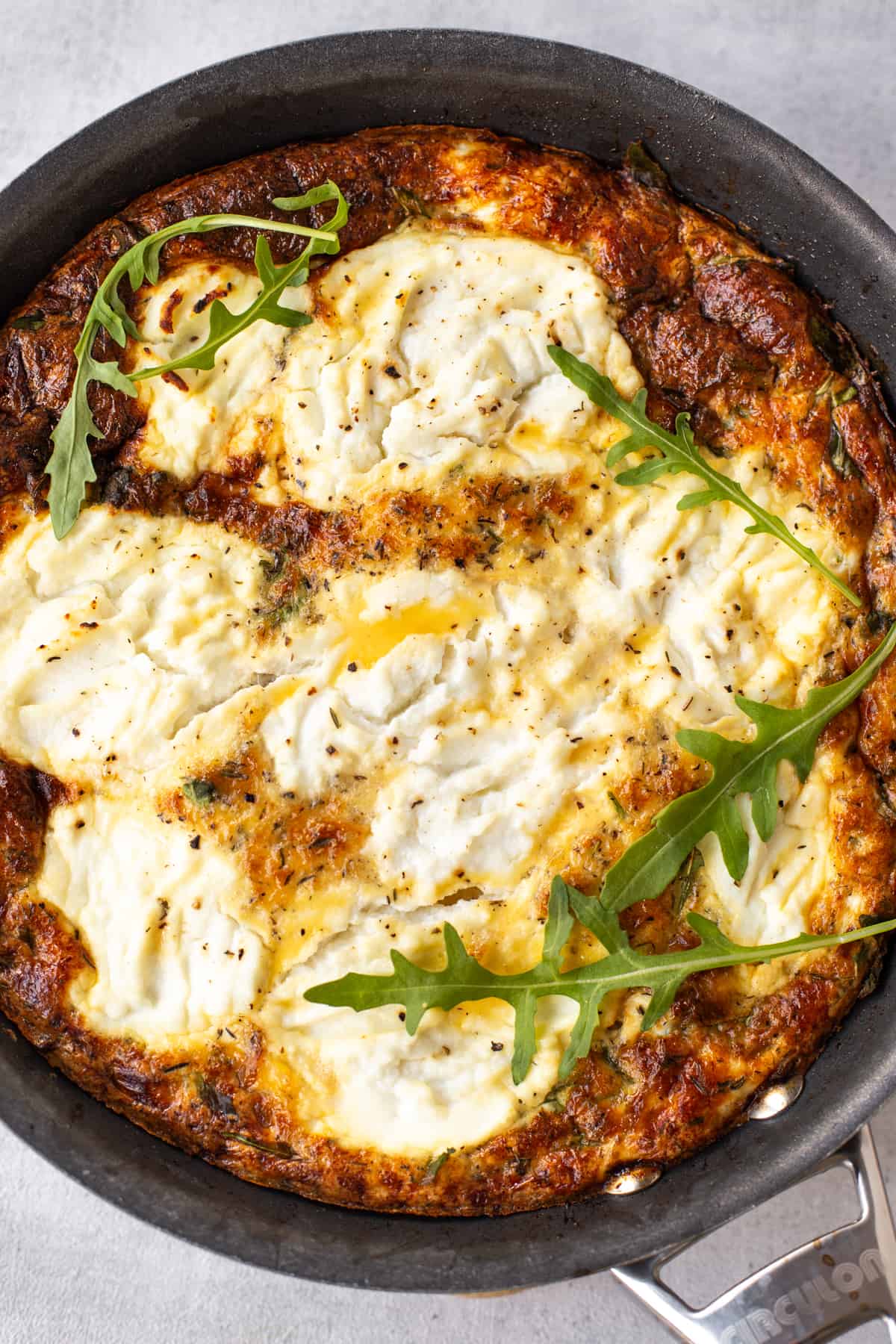 Caramelised onion and ricotta frittata in a pan with fresh rocket.
