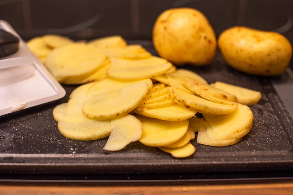 Thinly sliced potatoes on a chopping board.