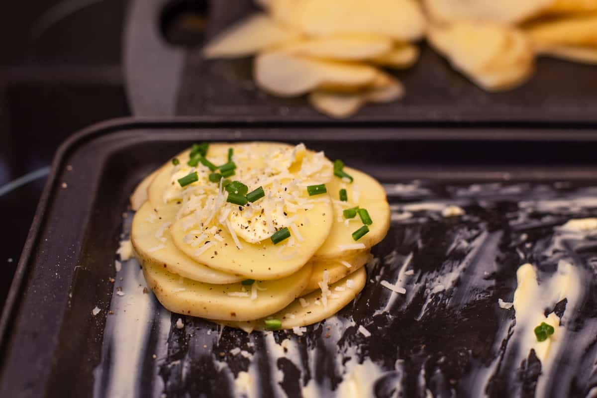 A stack of thinly sliced potatoes with parmesan, chives and butter.