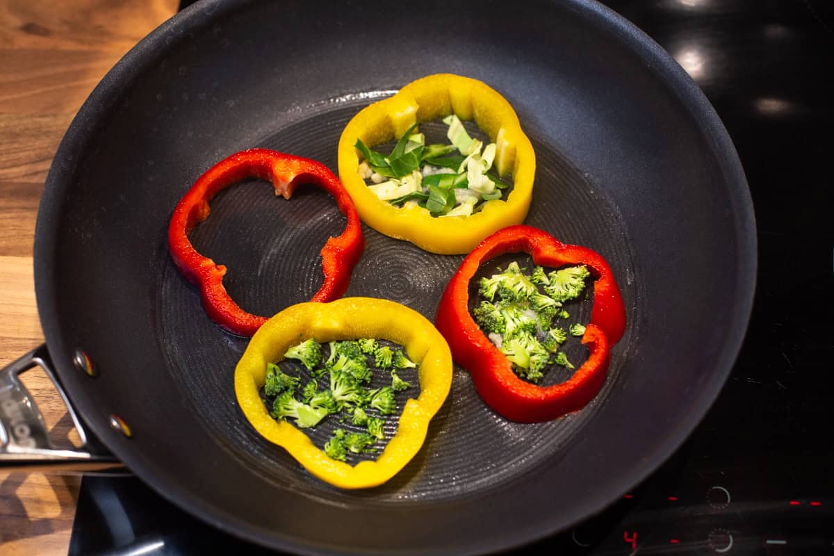 Rings of pepper in a frying pan with cabbage and broccoli inside.