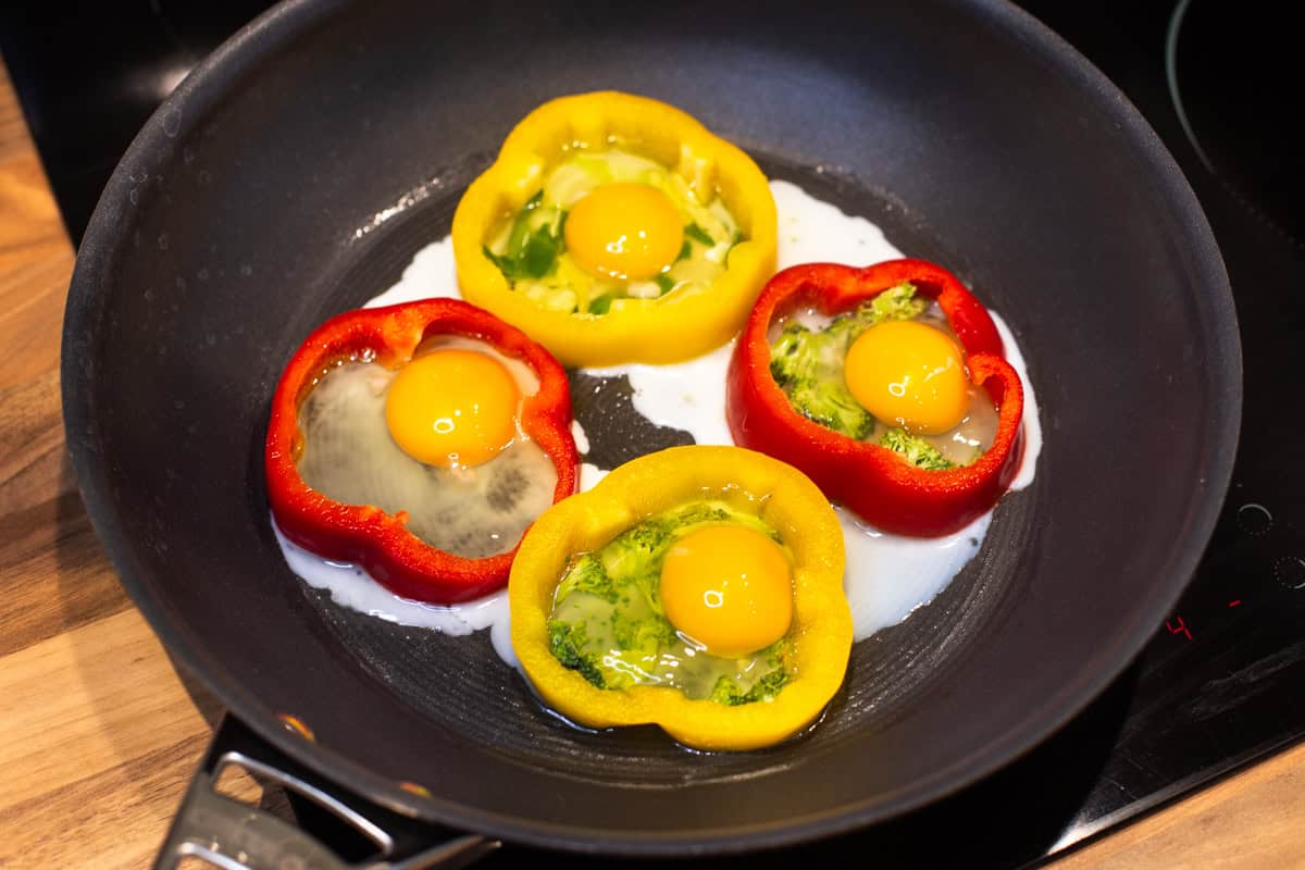 Raw eggs inside pepper rings in a frying pan.