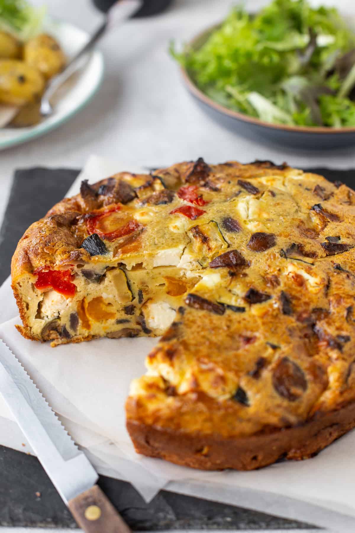 Vegetable and feta quiche with a slice removed.