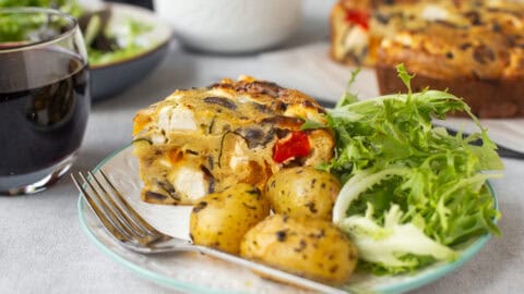 A slice of vegetable crustless quiche on a plate with baby potatoes and salad.