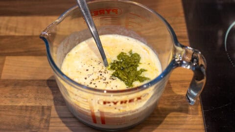 Beaten eggs in a jug with a dollop of pesto.