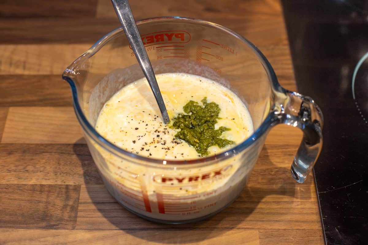 Beaten eggs in a jug with a dollop of pesto.