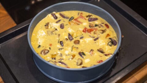 Uncooked crustless vegetable quiche in a springform cake tin.