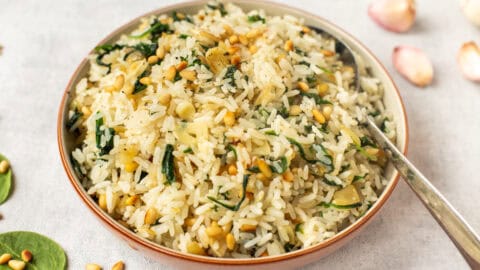 A bowl of garlic spinach rice topped with toasted pine nuts.
