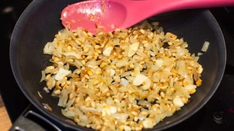 Fried onions, garlic and pine nuts in a frying pan.