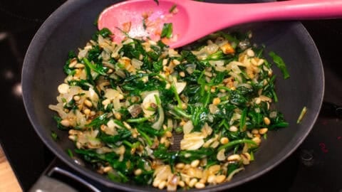 Sautéed spinach with garlic and pine nuts in a frying pan.
