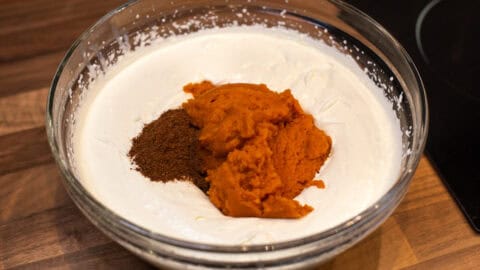 A large bowl of whipped cream topped with canned pumpkin and spices.