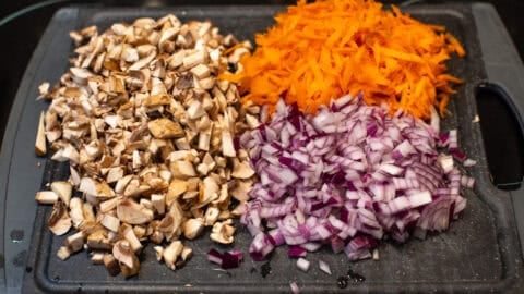 Finely chopped mushrooms, red onion and carrot on a cutting board.