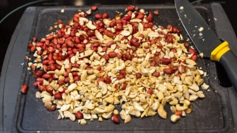 Chopped peanuts and cashew nuts on a cutting board.