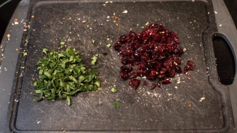 Chopped sage and dried cranberries on a cutting board.