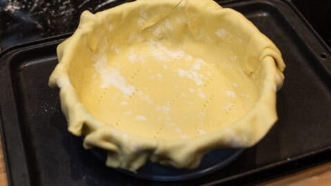 Uncooked shortcrust pastry draped over a cake tin.