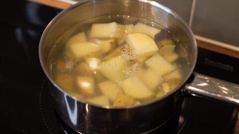 Pieces of potato cooking in a pan of water.