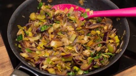 Sautéed leeks and red onion in a frying pan.