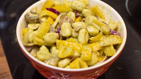 Gnocchi and raw vegetables coated in pesto in a mixing bowl.