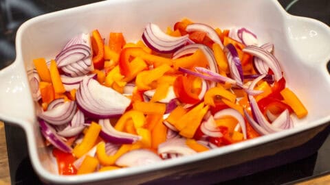 Chopped peppers and red onion in a large baking dish.
