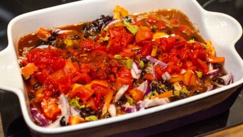 Uncooked rice, beans, vegetables and tomatoes in a baking dish.