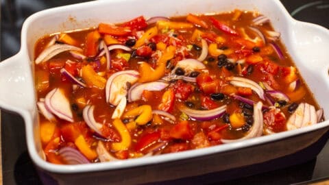 Uncooked rice, beans, vegetables and tomatoes in a baking dish.