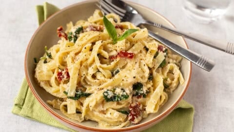 A bowl of creamy tofu pasta with spinach and sun-dried tomatoes.