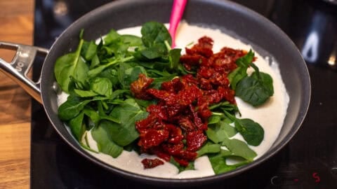 Creamy tofu sauce in a pan topped with chopped spinach and sun-dried tomatoes.