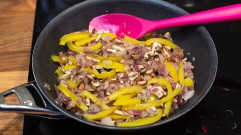Yellow pepper, mushrooms and red onion cooking in a frying pan.