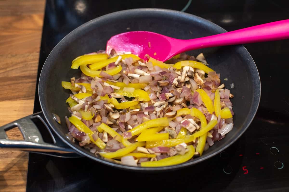 Yellow pepper, mushrooms and red onion cooking in a frying pan.