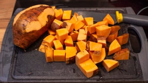 Diced sweet potato on a chopping board with some of the skin left on.