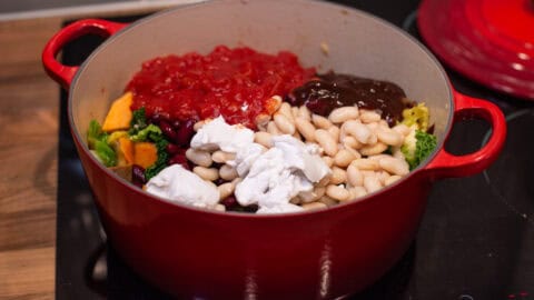 A large casserole dish with tomatoes, beans, and coconut milk inside.