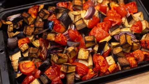 Roasted eggplant, tomatoes and red onion on a baking tray.