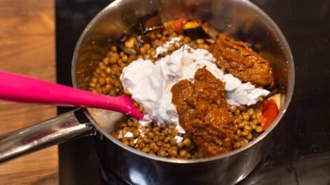 Canned lentils, coconut milk, curry paste and roasted vegetables in a saucepan.