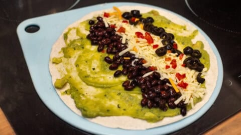 A flour tortilla topped with guacamole, black beans, cheese and olives.