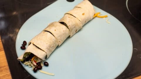 A stuffed tortilla rolled up on a board, cut into pieces.