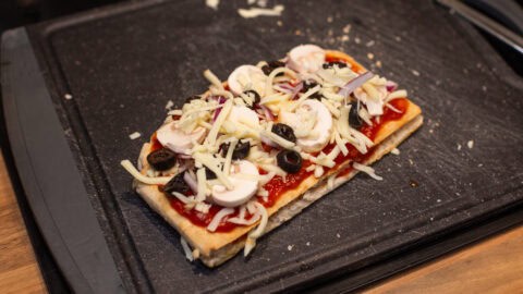 Pitta bread topped with cheese and vegetables on a board.