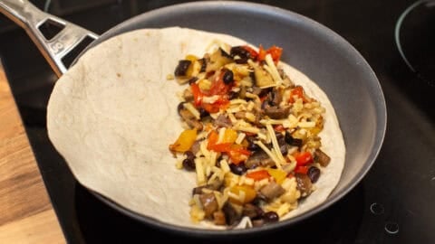 A tortilla in a frying pan filled with roasted vegetables and cheese.