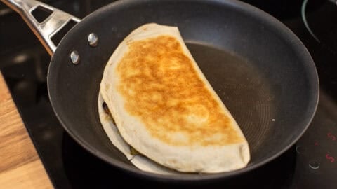 A crispy quesadilla cooking in a frying pan.