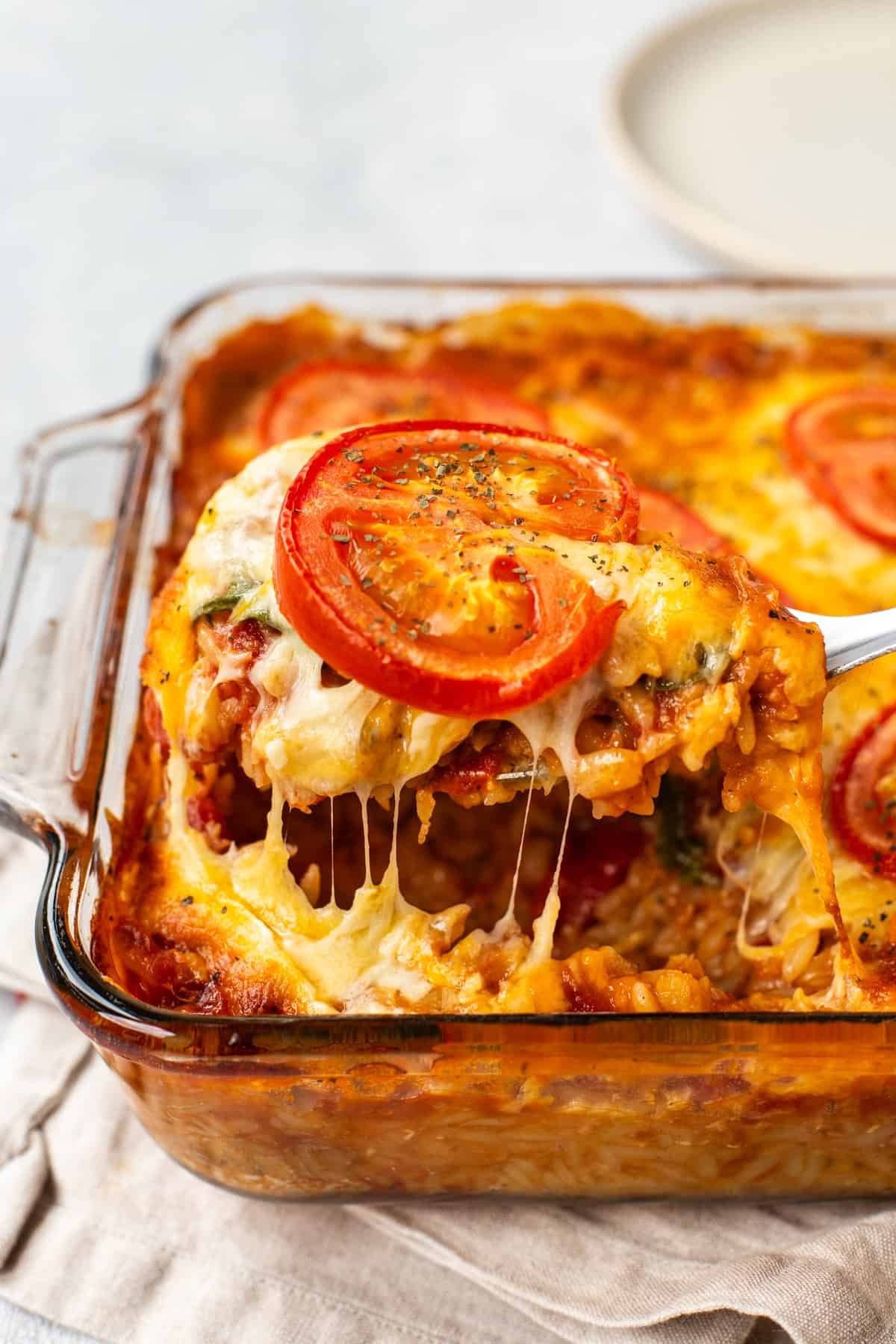 A spoon taking a scoop of cheese and tomato baked orzo in a dish.