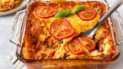 A baking dish of cheese and tomato baked orzo with a scoop removed.