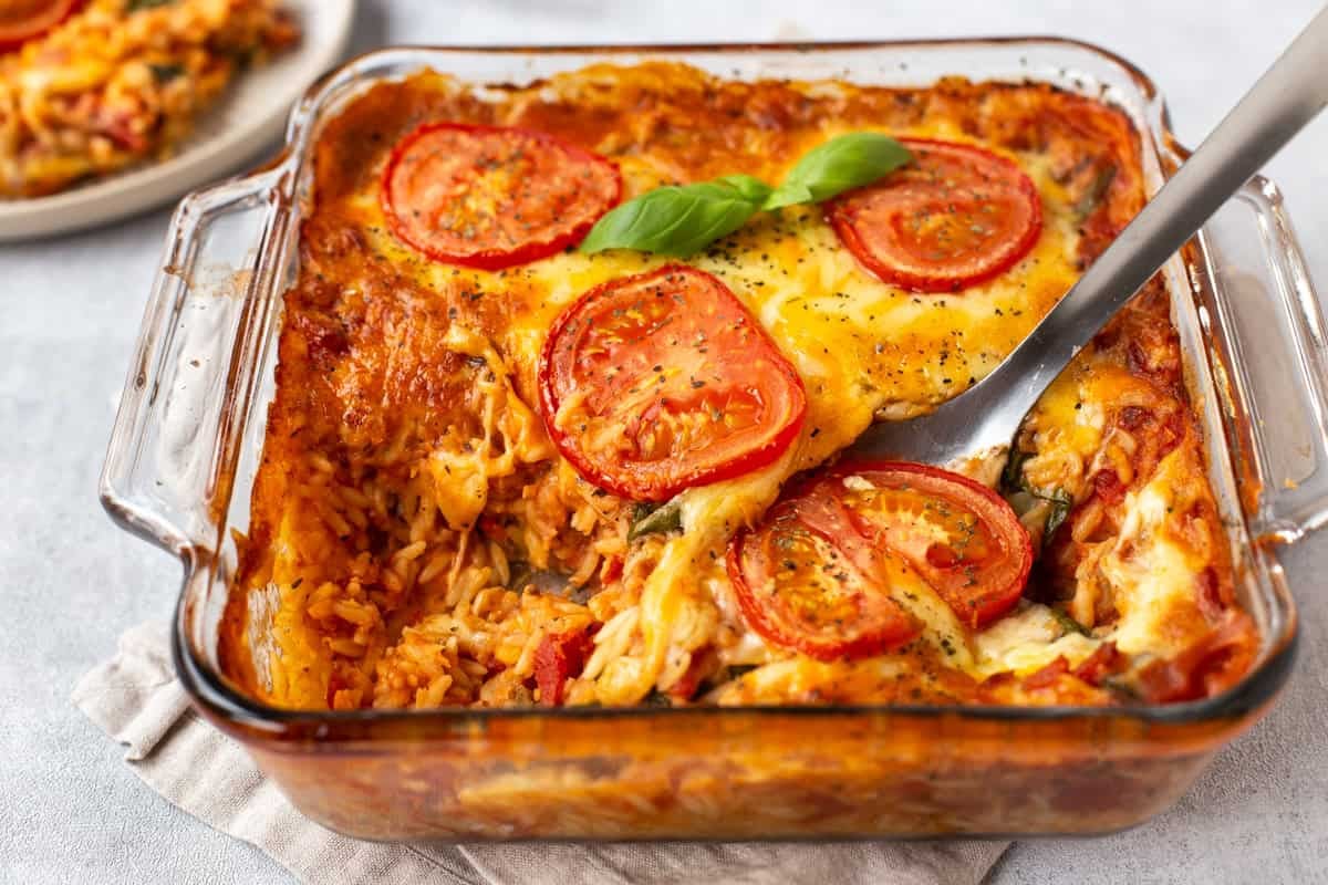 A baking dish of cheese and tomato baked orzo with a scoop removed.