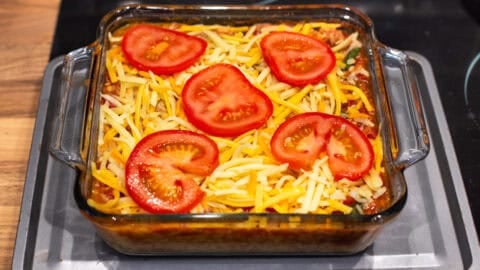 Baked orzo in a baking dish topped with grated cheese and slices of tomato.