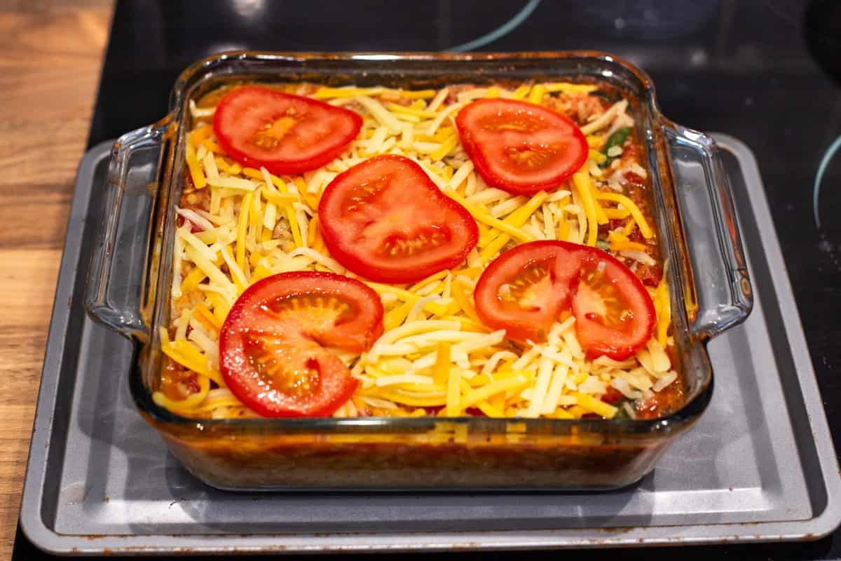 Baked orzo in a baking dish topped with grated cheese and slices of tomato.