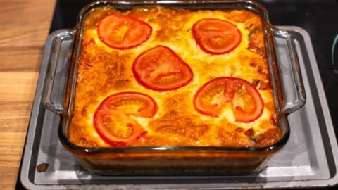 Crispy cheese and tomato baked orzo in a baking dish topped with sliced tomatoes.