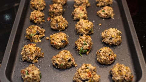 Uncooked vegetarian Mediterranean lentil meatballs laid out on a baking sheet.